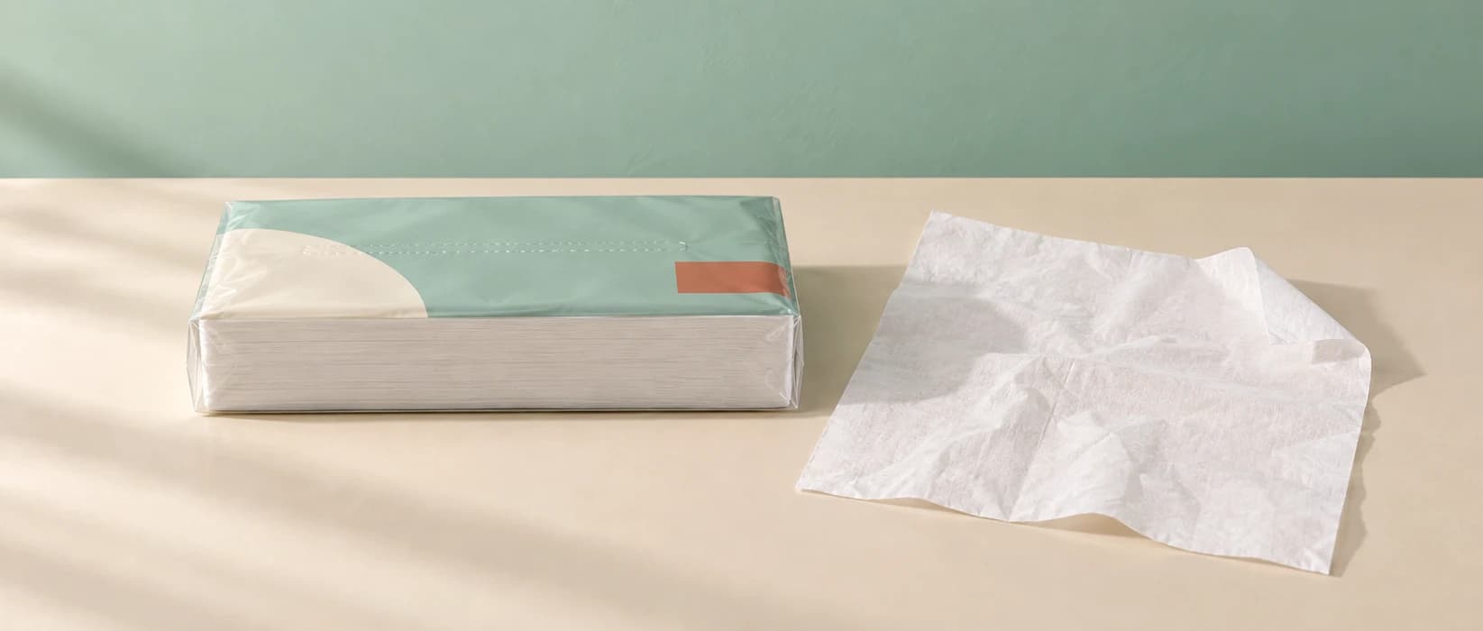 Concept scene of a mint-green flexible-film facial tissue pack beside an unfolded white tissue
