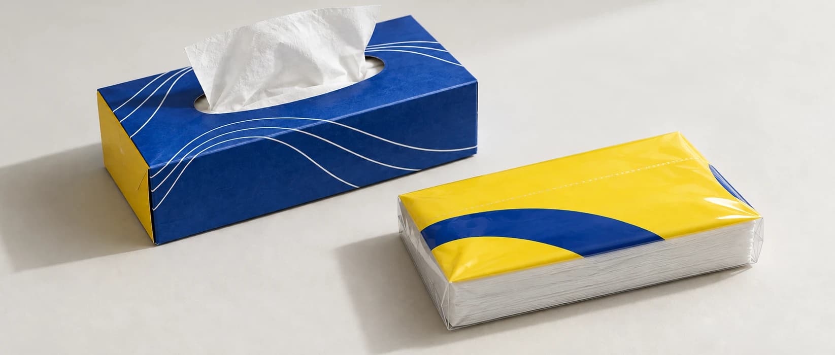 Concept comparison of a blue folding tissue carton and a low yellow-topped tissue stack in clear flexible film