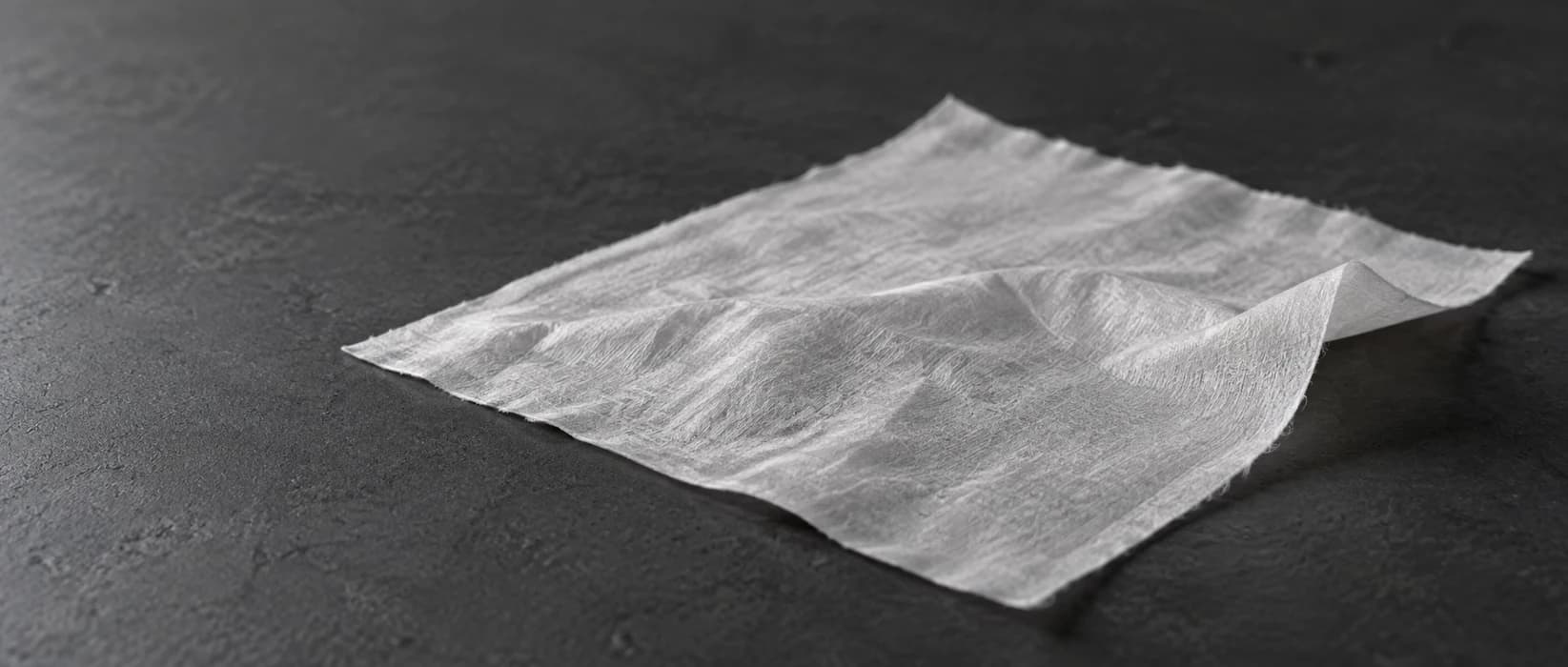 Close concept view of white facial tissue with a gently curled edge on a charcoal surface