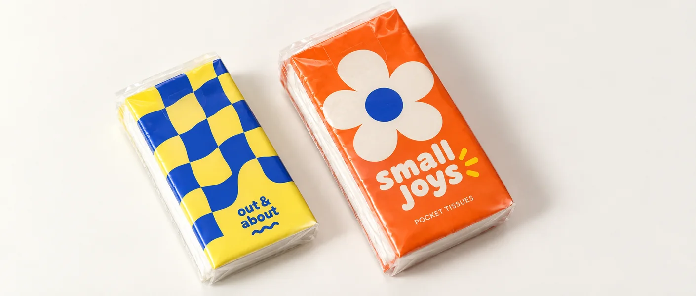 Two original pocket tissue designs with orange floral and blue checker graphics on small sealed film packs