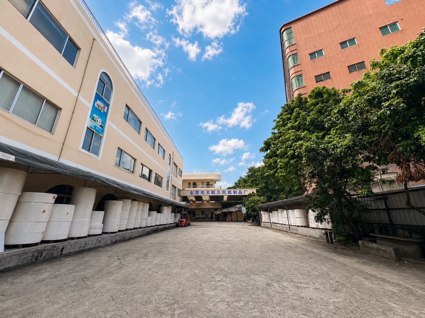 Exterior courtyard of Dongguan Dalang Jiufeng Paper Products Factory with wrapped parent tissue rolls and the factory sign